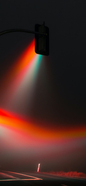 Cinematic traffic light beams shining through thick fog at night on a dark road.