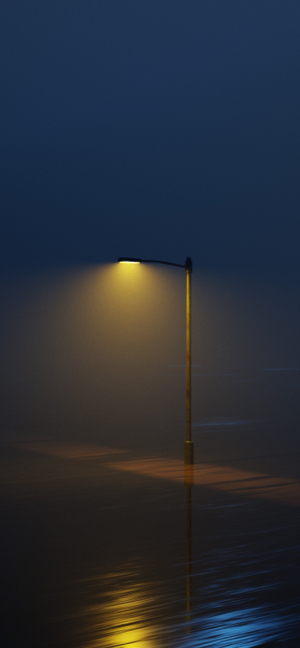 A single street lamp glowing with warm yellow light in a thick, dark blue fog over a reflective wet ground.