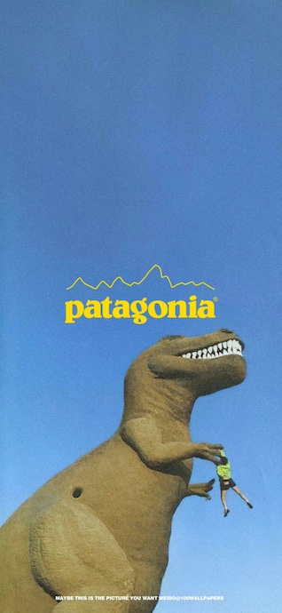 A large Tyrannosaurus Rex statue with a yellow Patagonia logo above it against a clear blue sky, with a small person hanging from its arm.