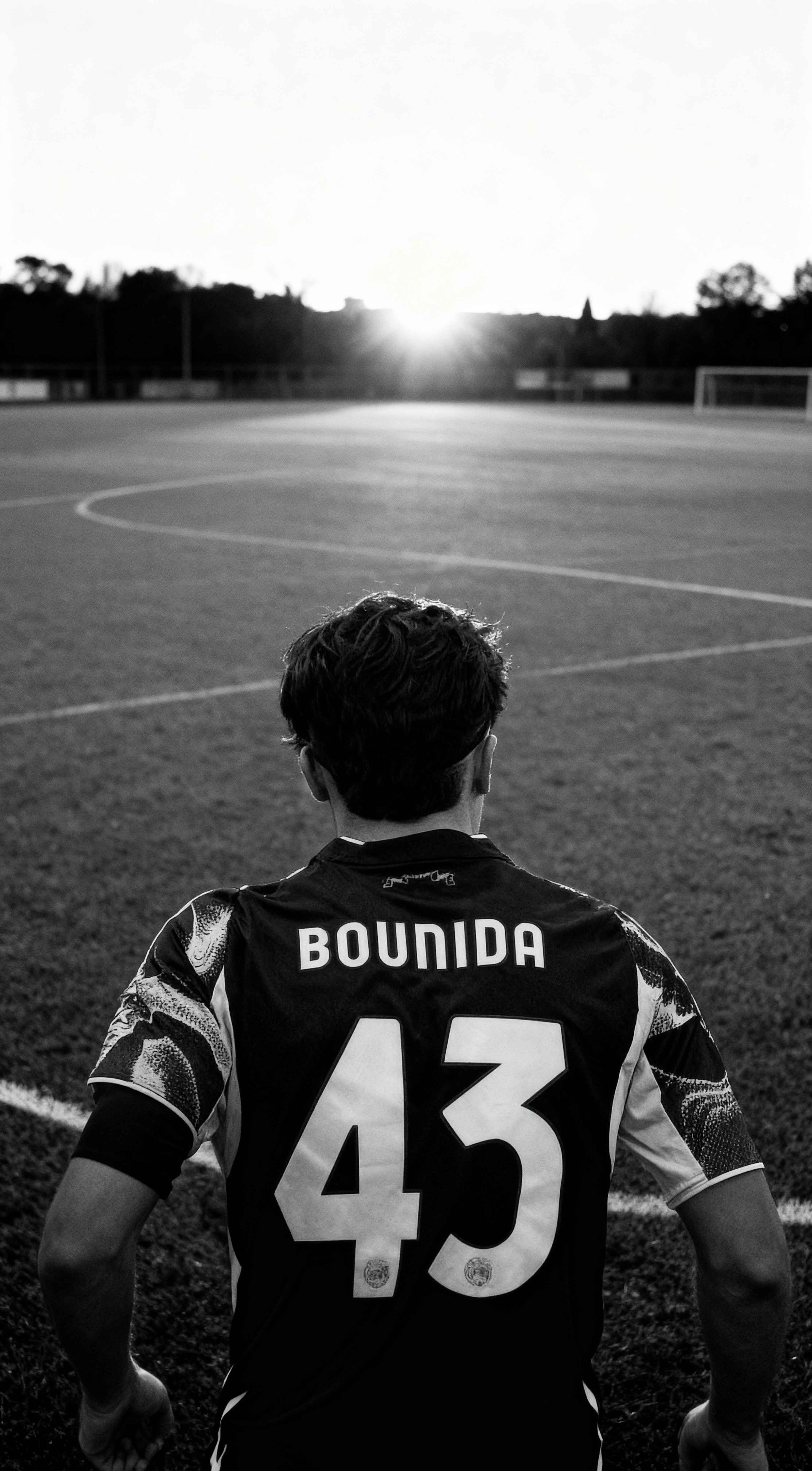 Black and white photo of football player Rayane Bounida from behind on a pitch, wearing number 43 jersey at sunset.