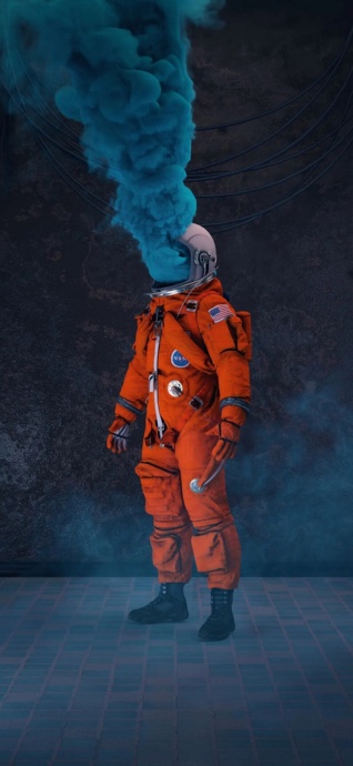 An astronaut in an orange NASA suit with thick blue smoke billowing from the helmet visor against a dark, textured wall background.