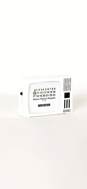 A minimalist white 3D object shaped like a vintage retro television featuring the Maison Martin Margiela numeric branding and 'Invitation' text on the screen against a white background.