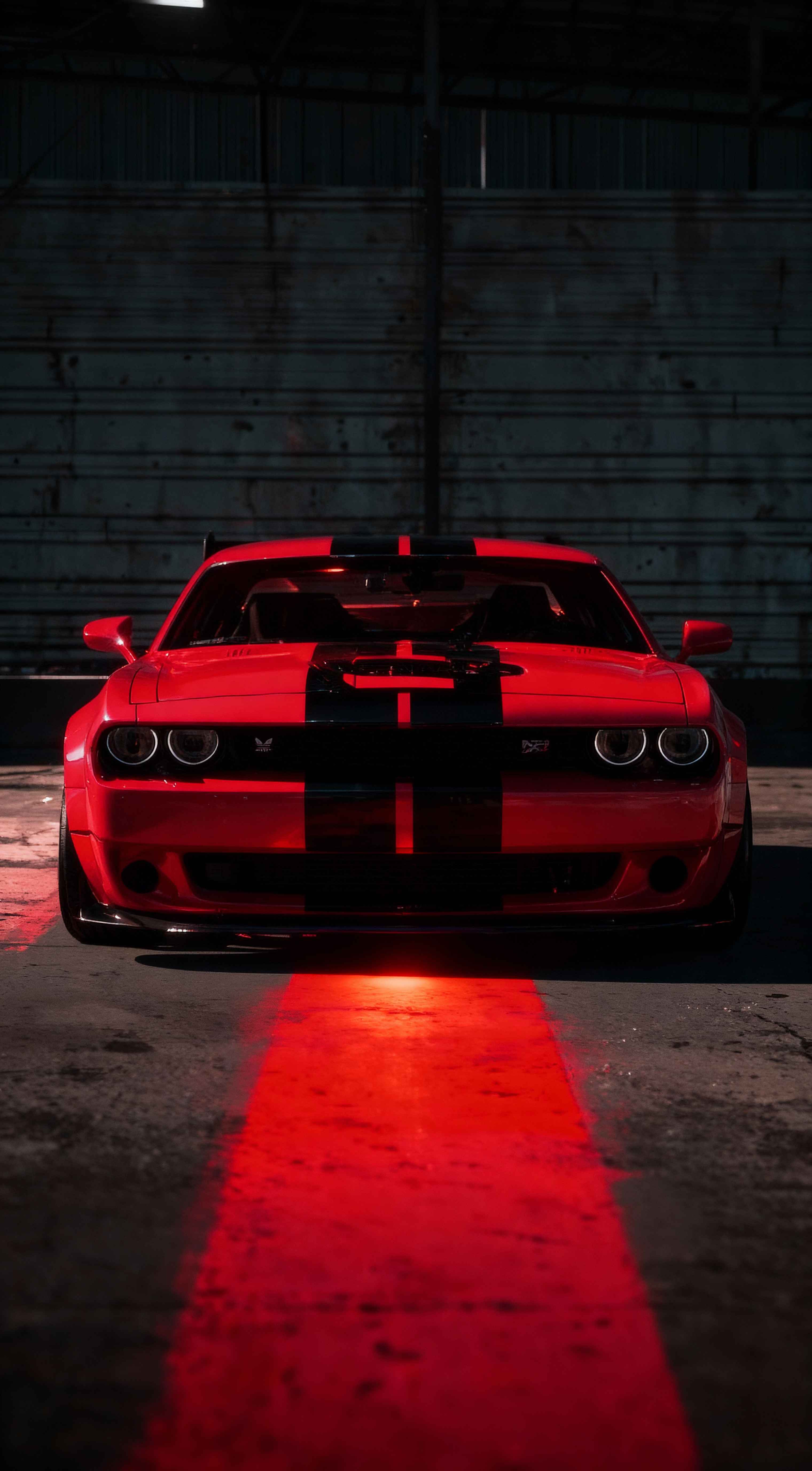Front view of a red Dodge Challenger with black stripes in a dark garage, red light reflecting on the ground.