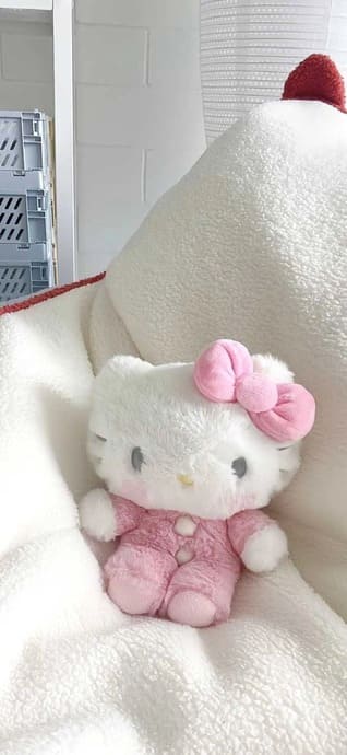 Une peluche Hello Kitty avec un pyjama rose et un nœud rose sur une couverture blanche duveteuse.