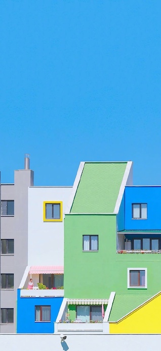 Low angle shot of colorful, geometric modern apartments in green, blue, and yellow under a clear bright blue sky.