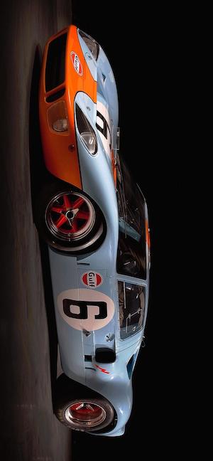 Side profile of a classic Ford GT40 race car with the iconic light blue and orange Gulf Oil livery, set against a dark, dramatic background.