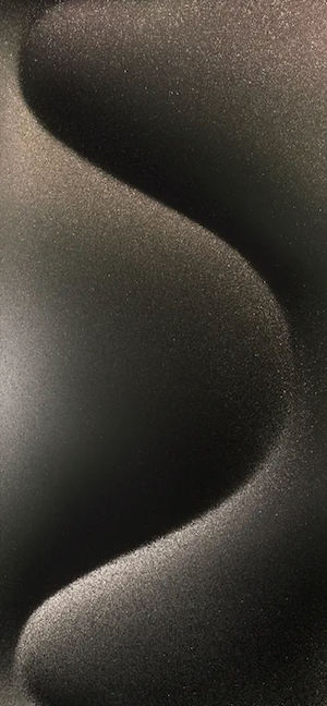 부드러운 조명 아래 S자형 곡선과 미세한 입자 질감이 있는 어두운 금속 표면의 클로즈업.