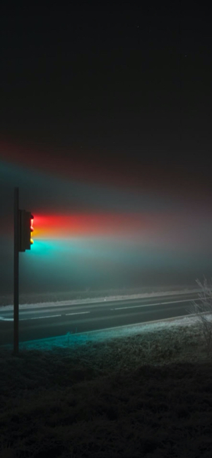 안개 낀 밤의 도로에서 빨강, 노랑, 초록 빛을 내뿜는 신호등.