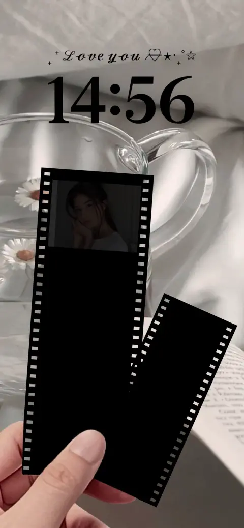 A hand holding a customizable film strip wallpaper template featuring black photo frames, a glass of water with daisies, and a romantic text overlay.