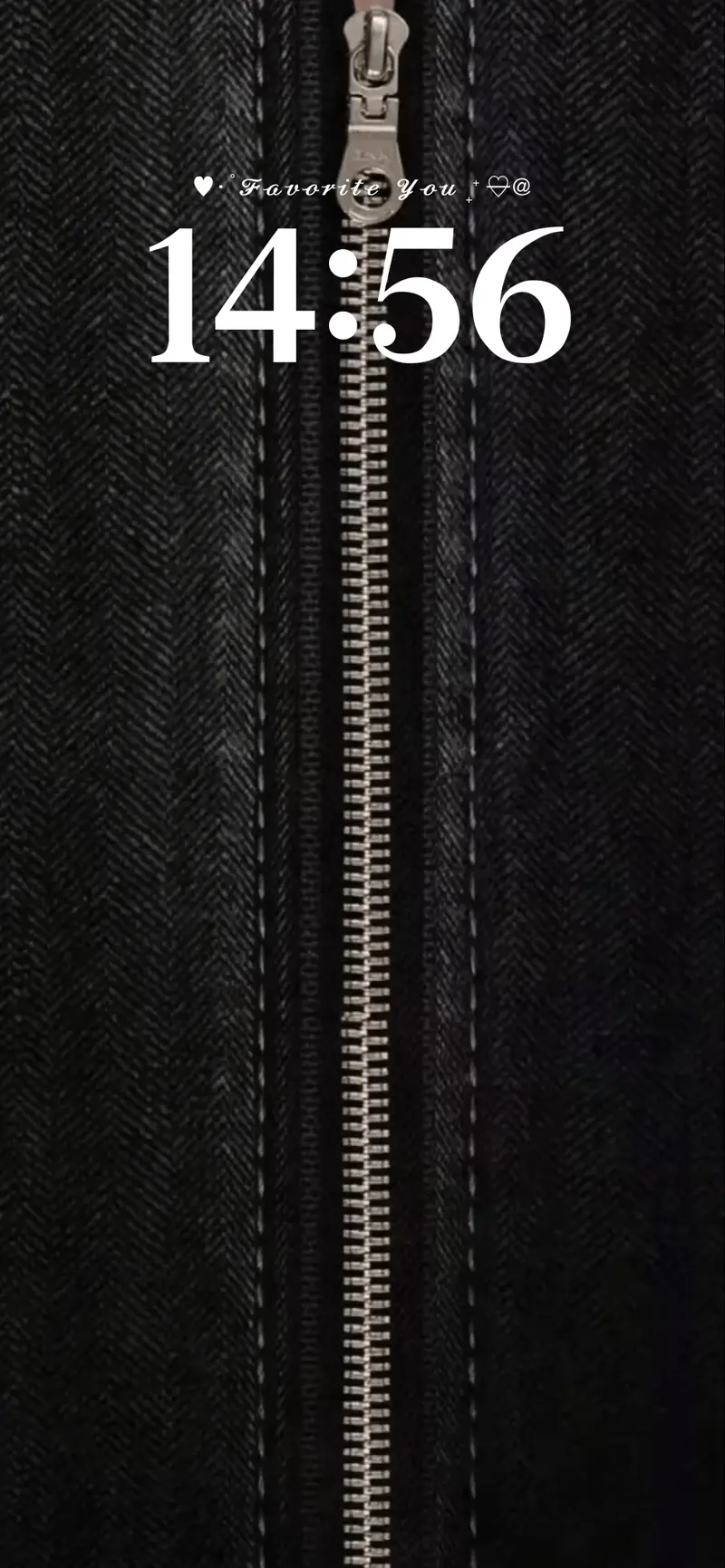 A close-up of a black denim fabric texture with a vertical silver metallic zipper and a white digital clock display.