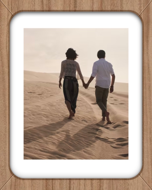 Couple walking on sand dunes inside a white rounded frame with a wooden texture background.