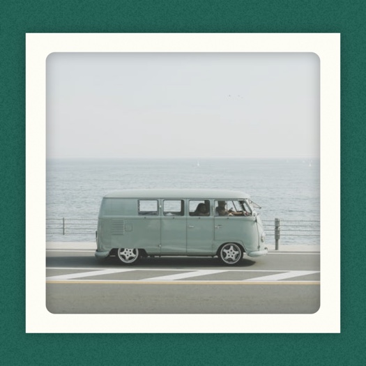 Vintage blue van driving by the ocean in a white polaroid frame against a dark green textured background.