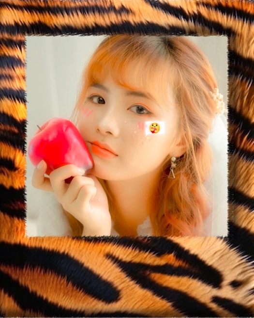 A photo of a girl with orange hair holding a red apple, framed by a thick, fuzzy tiger-print faux fur border with orange and black stripes.